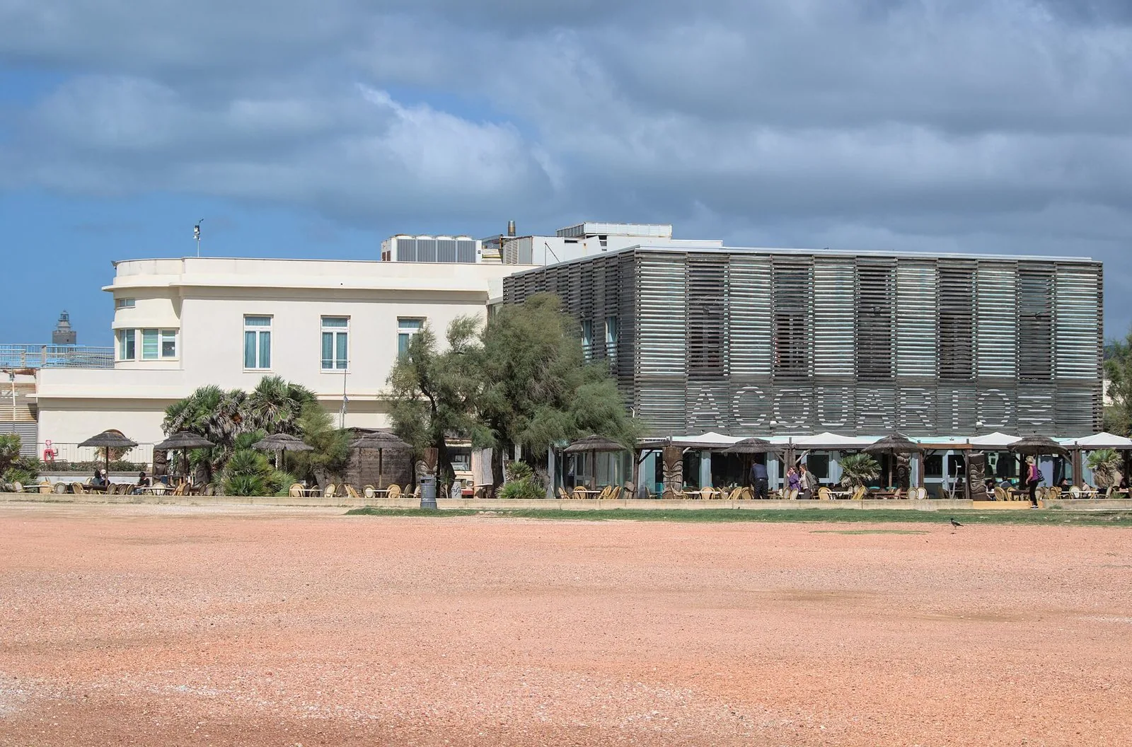 L’edificio dell’Acquario di Livorno sul lungomare, con l’ala bianca storica e il volume rivestito di listelli di legno con la scritta Acquario, sotto un cielo nuvoloso
