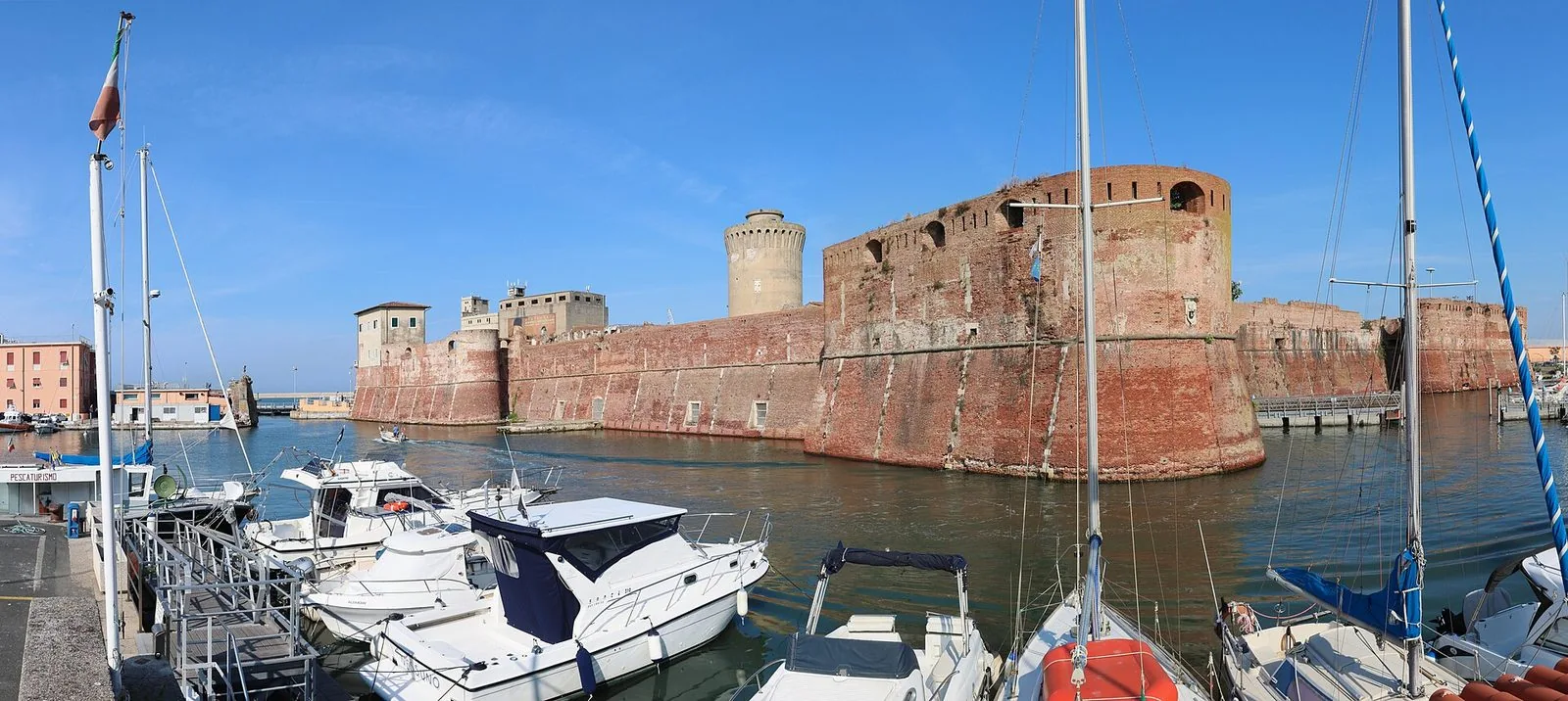 Le mura in mattoni della Fortezza Vecchia di Livorno con il torrione circolare, affacciate sull’acqua del porto mediceo con barche ormeggiate in primo piano