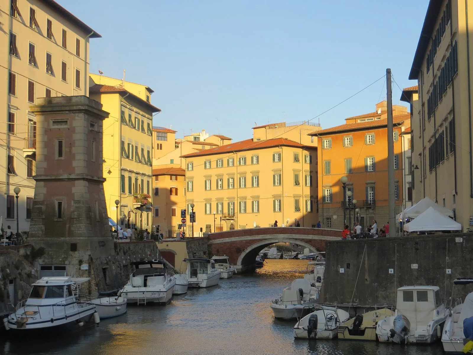 Un fosso del quartiere Venezia Nuova a Livorno al tramonto, con barche ormeggiate, un ponte in mattoni e palazzi color ocra illuminati dal sole
