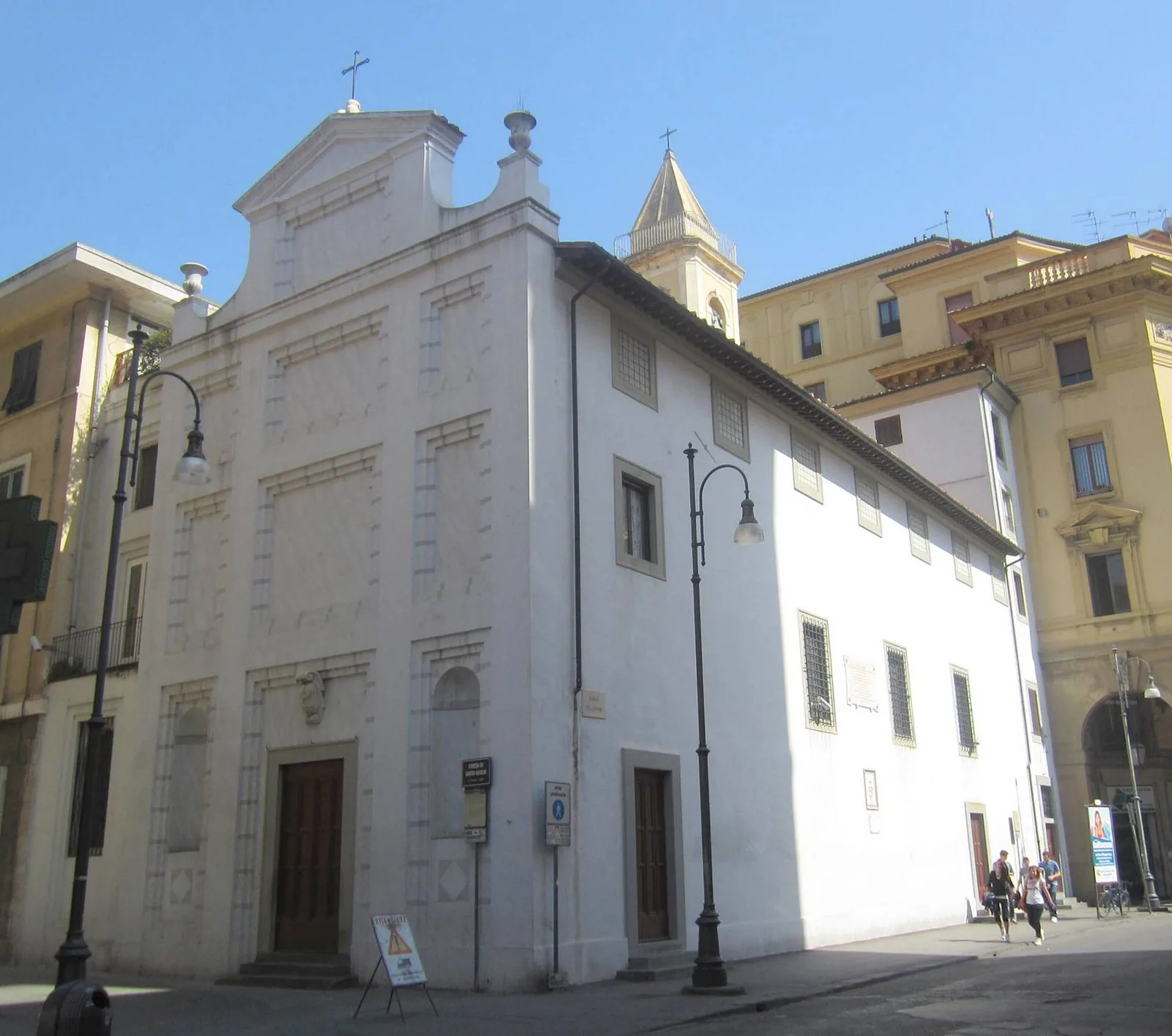 La facciata chiara della chiesa di Santa Giulia a Livorno, con il piccolo campanile e i lampioni della strada sotto un cielo azzurro