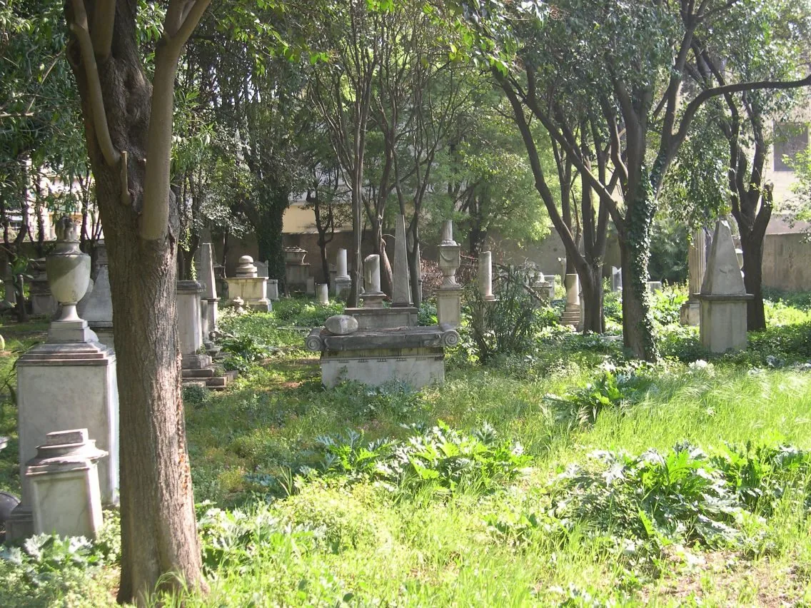 Monumenti funebri e urne in marmo tra alberi e prato nell'antico cimitero degli Inglesi di Livorno, illuminato dal sole