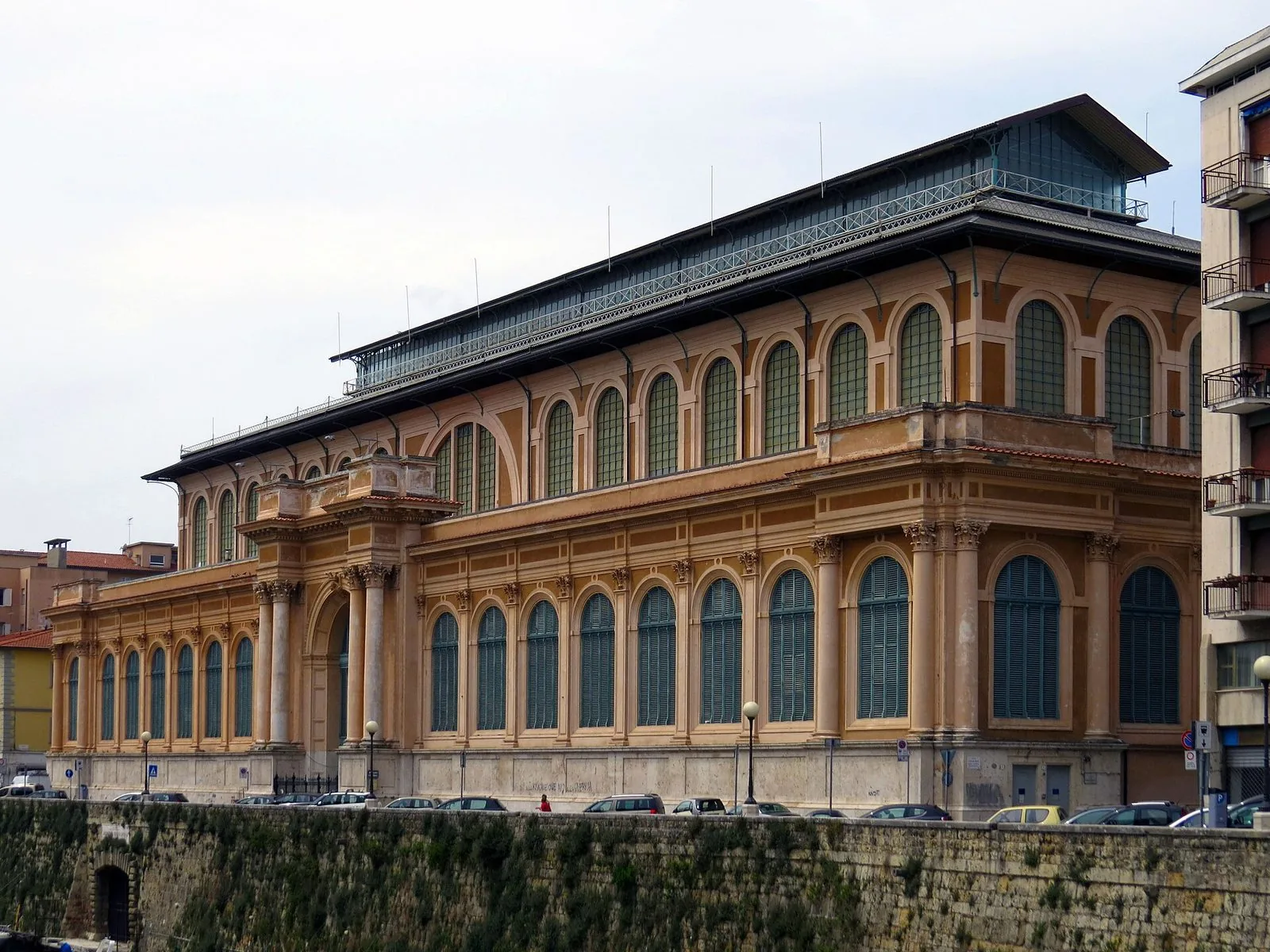 La lunga facciata ottocentesca del Mercato delle Vettovaglie di Livorno, con finestre ad arco, colonne e il tetto in ferro e vetro, vista dal muro del Fosso Reale