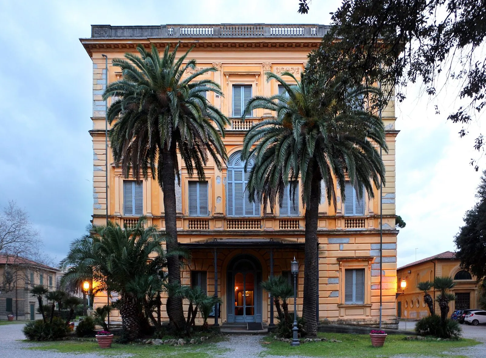 La facciata color ocra di Villa Mimbelli a Livorno, con persiane azzurre e balaustre, incorniciata da due grandi palme davanti all’ingresso